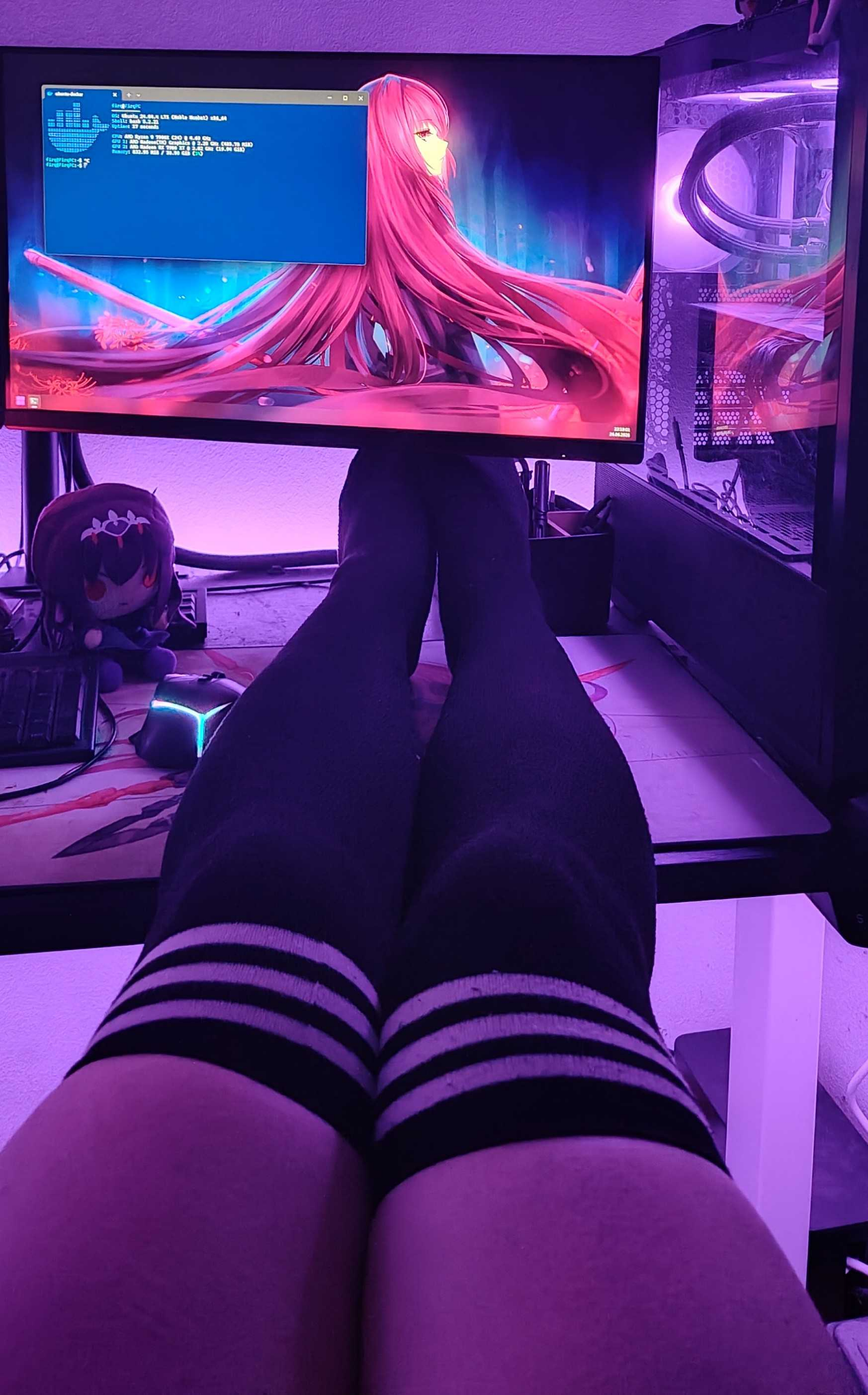 First-person view of legs wearing black thigh-high socks with three white stripes at the top, resting on a computer desk. The entire setup is bathed in a purple and pink neon glow. On the desk, a gaming mouse glows with cyan light next to a small plushie of Scathach-Skadi from Fate/Grand Order. The computer monitor displays a desktop background of a red-haired anime girl with a blue terminal window opened, showing a fastfetch screen with a docker logo.

To the right of the monitor, a PC tower with illuminated purple fans is visible.