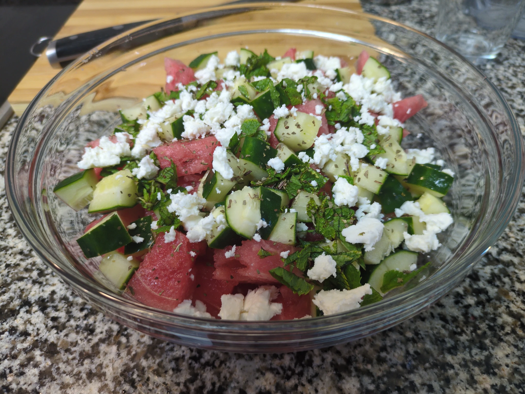 A bowl of sliced watermelon and cucumber, with crumbled feta cheese, chopped mint, and dried basil flakes